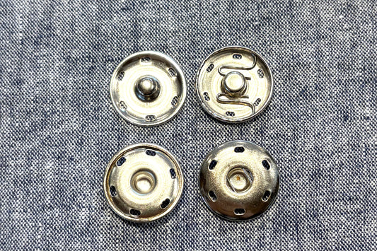 Four metallic snap pieces on a textured fabric background